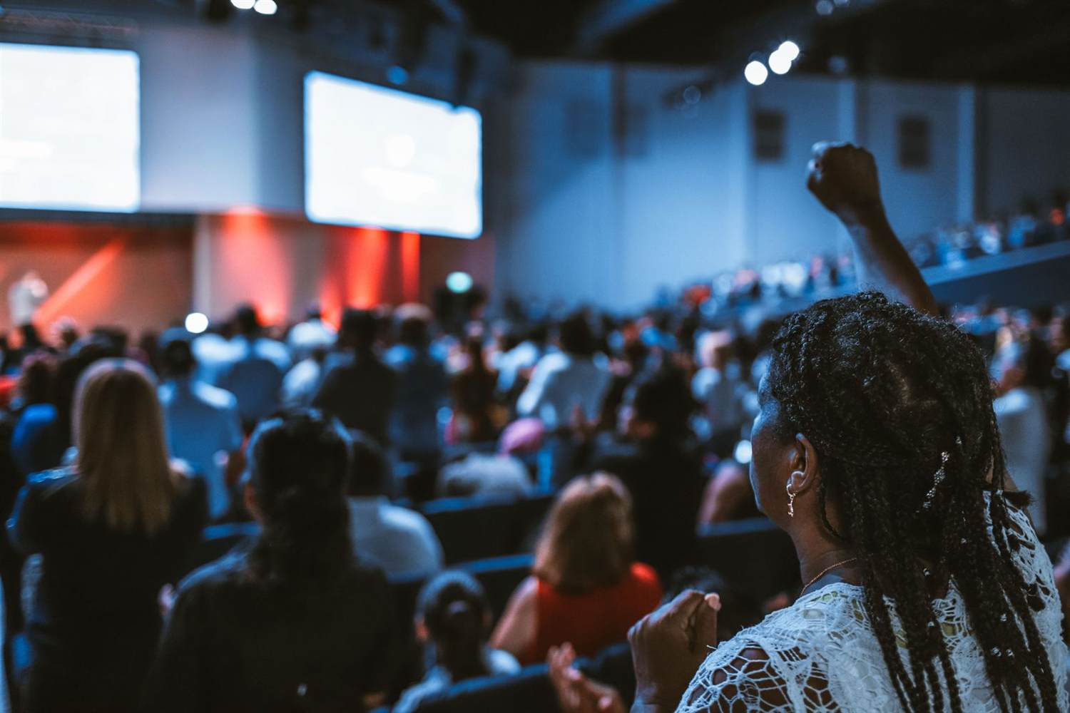 An attendee raises a fist in a packed conference hall facing two large screens
