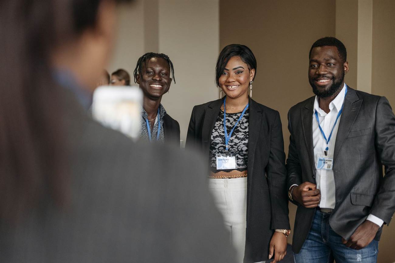 Three smiling attendees wearing conference badges being photographed at an event