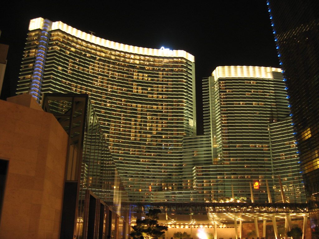 The two curved glass towers of ARIA Resort & Casino lit at night above the main entrance canopy at CityCenter