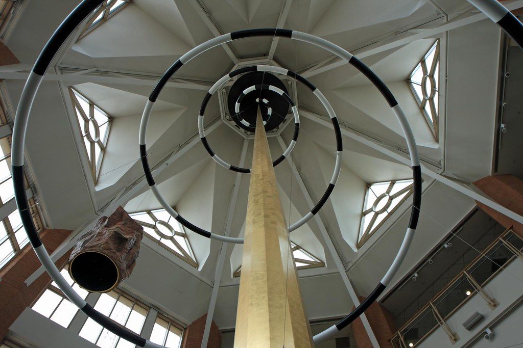 Looking up into an entrance rotunda of the Milwaukee convention center, with black-and-white rings and a gilded spire suspended under the skylit roof