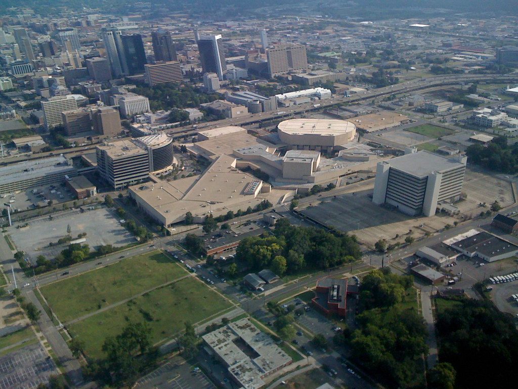 Aerial view of the BJCC campus in downtown Birmingham, Alabama: the round arena roof, the low exhibition hall roofs and a hotel tower, with the city center behind