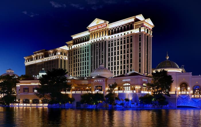 Caesars Palace lit up at night, its towers and domes reflected in the lake in front of the resort