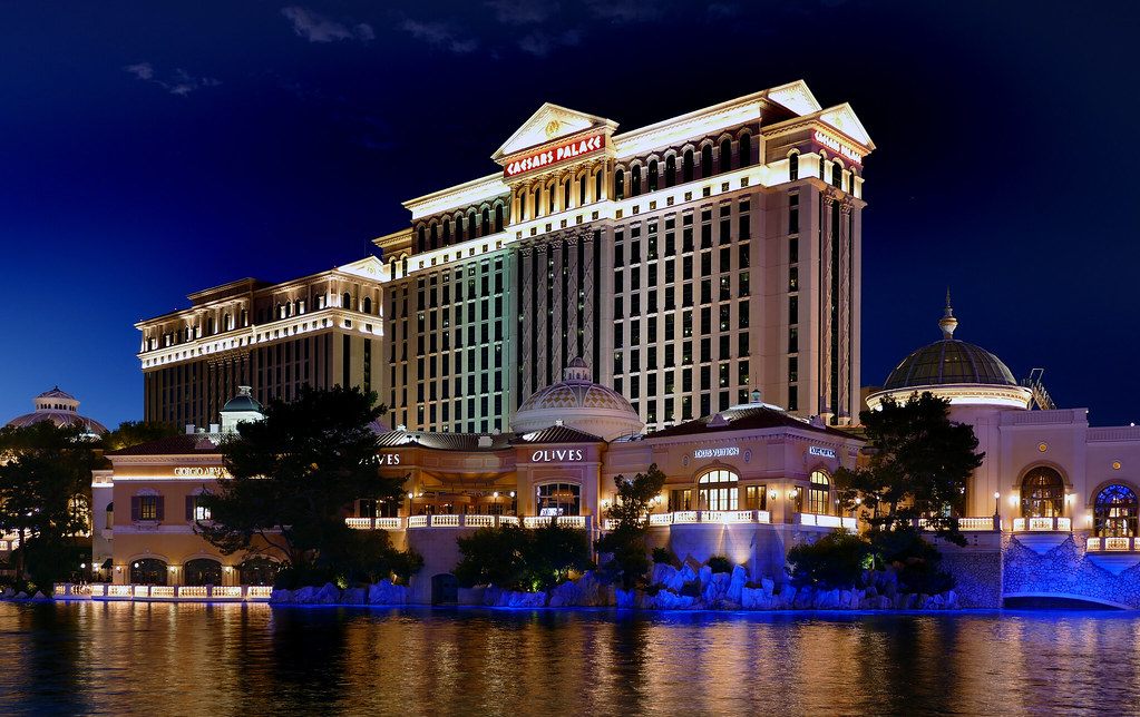 Caesars Palace lit up at night, its towers and domes reflected in the lake in front of the resort