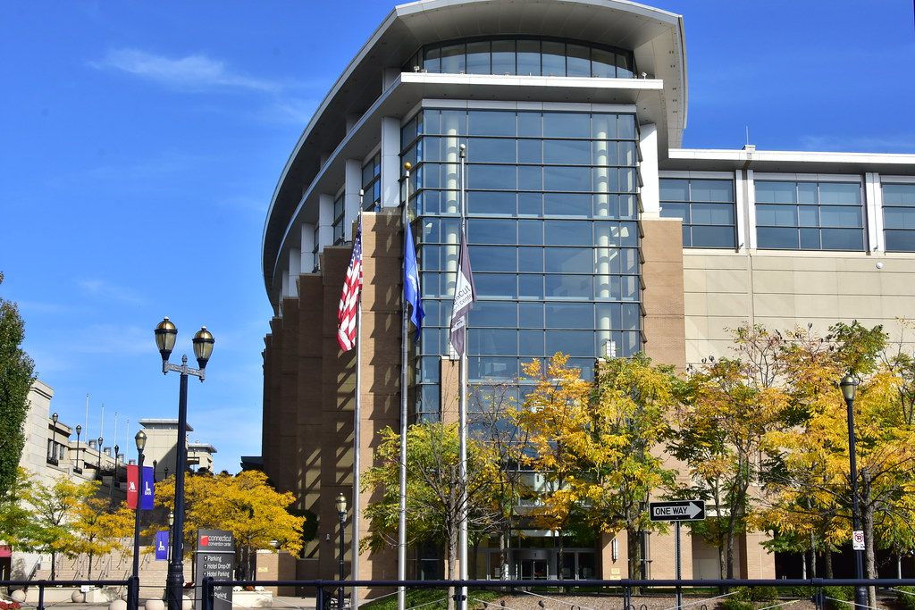 The curved glass and stone front of the Connecticut Convention Center in Hartford, with flags and autumn trees along the plaza