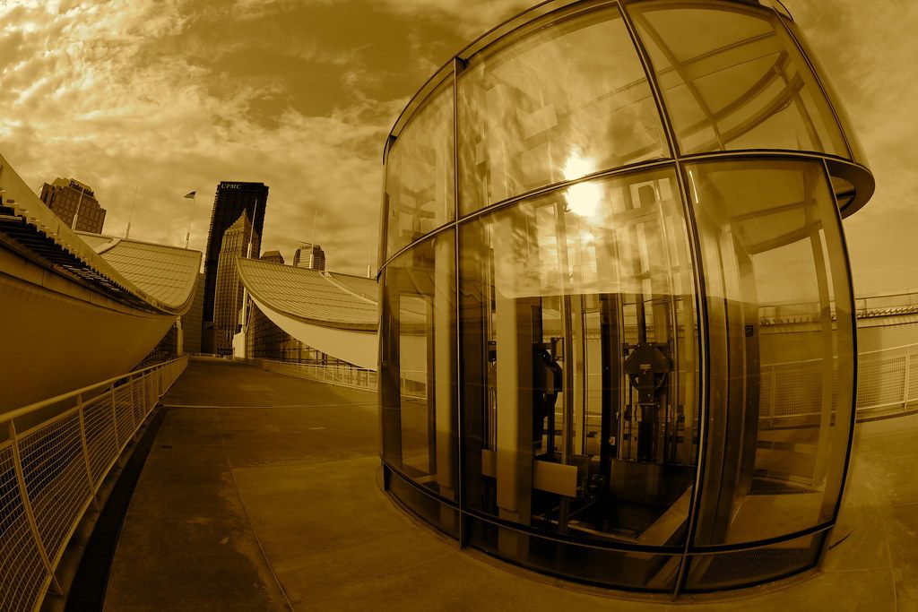 A glass elevator enclosure on the convention center's rooftop with the roof bays and downtown towers behind