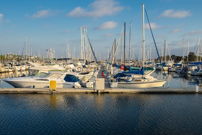 Sailboats and motor yachts moored along a floating dock in a Chula Vista marina in soft evening light, under a blue sky