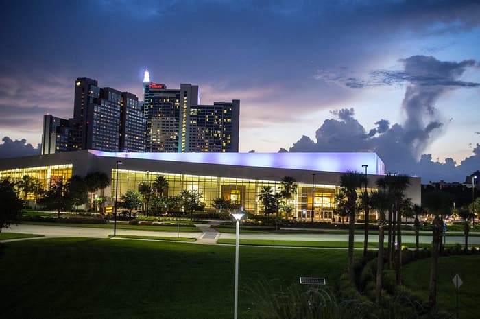 The hotel towers, lit at dusk with The Peabody sign on top, rising behind a low glass hall and palm-lined lawns on International Drive
