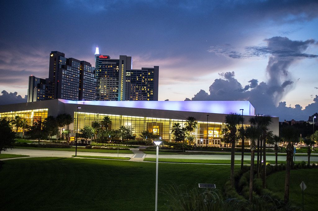 The hotel towers, lit at dusk with The Peabody sign on top, rising behind a low glass hall and palm-lined lawns on International Drive