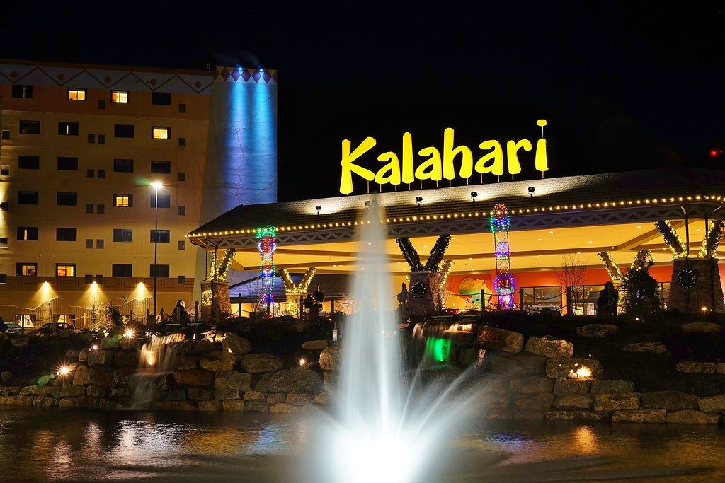 The lit Kalahari sign over the main entrance canopy of Kalahari Resorts in the Poconos at night, with a fountain in the foreground and the hotel wing to the left