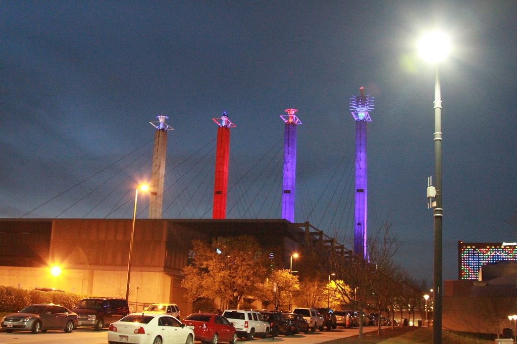 The four Bartle Hall pylons lit red, purple and blue at dusk, with their Sky Station sculptures on top and the roof cables fanning down to the convention hall