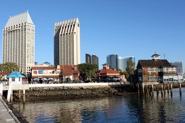 The two Manchester Grand Hyatt towers rising behind the red-roofed shops of Seaport Village on the San Diego Bay waterfront under a clear blue sky