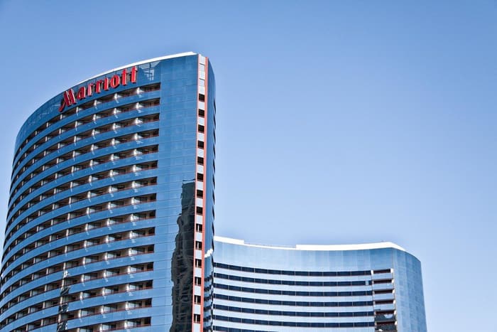 The two curved blue-glass towers of the Marriott Marquis San Diego Marina, the taller one topped with a red Marriott sign, against a clear blue sky