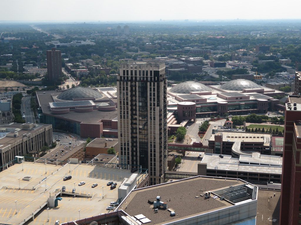 Aerial view of the southern edge of downtown Minneapolis, with the domed roofs of the Minneapolis Convention Center beside a dark residential tower