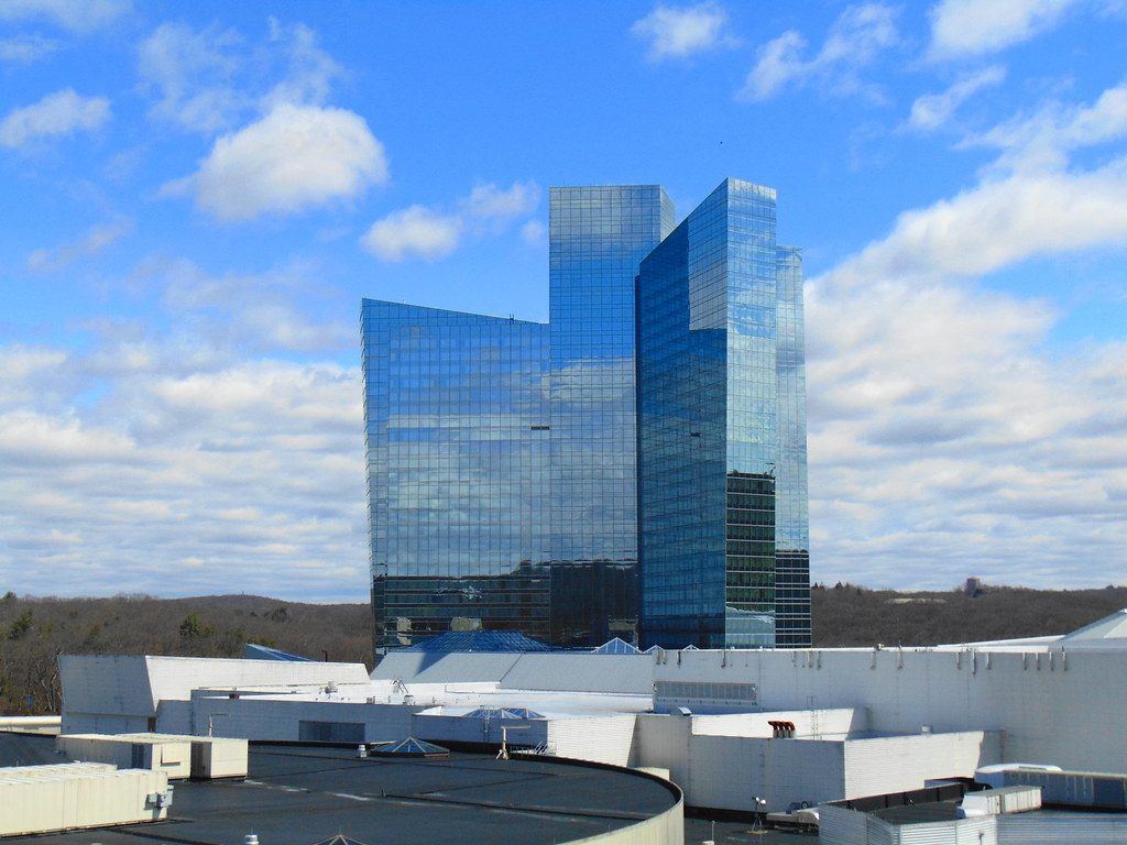 The glass Sky Tower of Mohegan Sun in Uncasville rising above the resort roofs under a blue sky with clouds