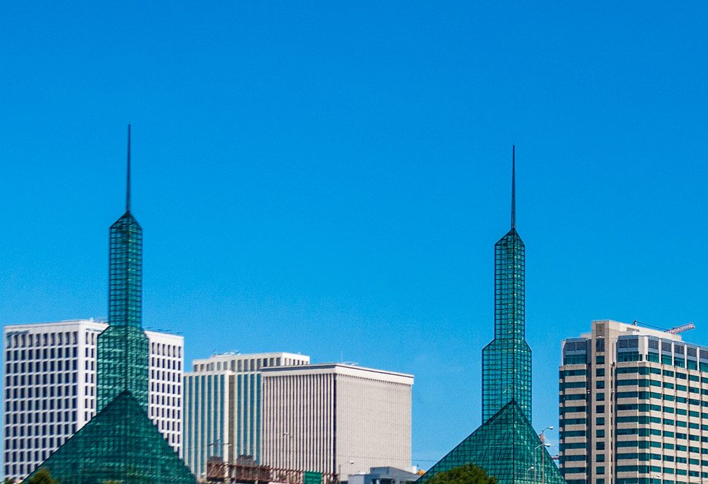 The twin green glass spires of the Oregon Convention Center against a blue sky, with Lloyd District office towers behind