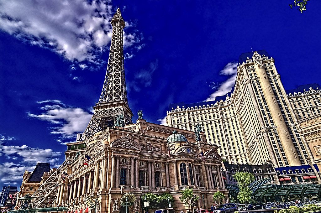 The half-size Eiffel Tower replica rising behind the ornate Paris Las Vegas façade, with the cream hotel tower at right under a deep blue sky