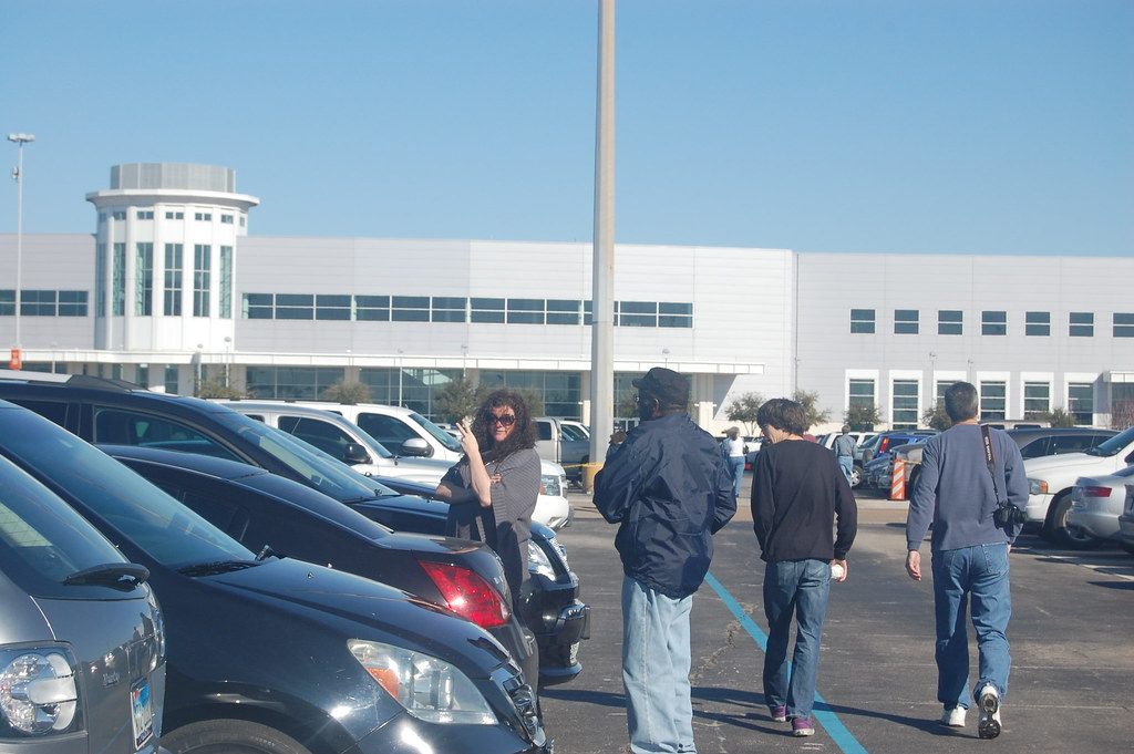 The long white front of Reliant Center with its round glass entrance tower, seen across a parking lot as visitors walk toward the doors