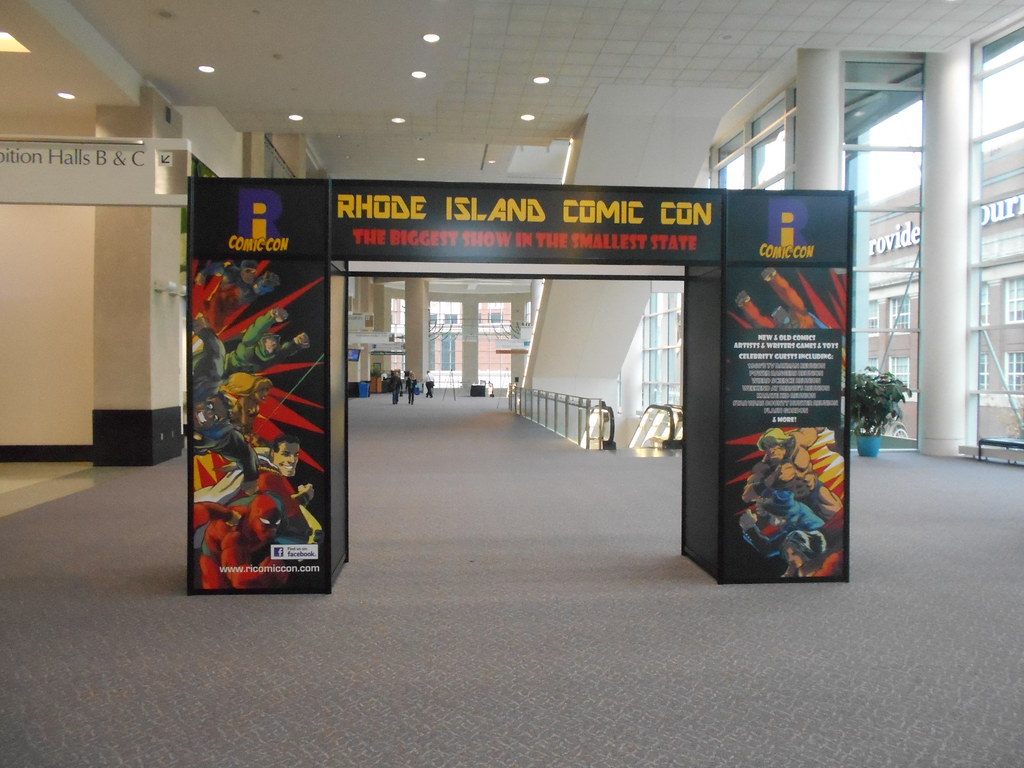 The carpeted upper concourse of the Rhode Island Convention Center, with a Rhode Island Comic Con entrance arch and a sign to Exhibition Halls B and C