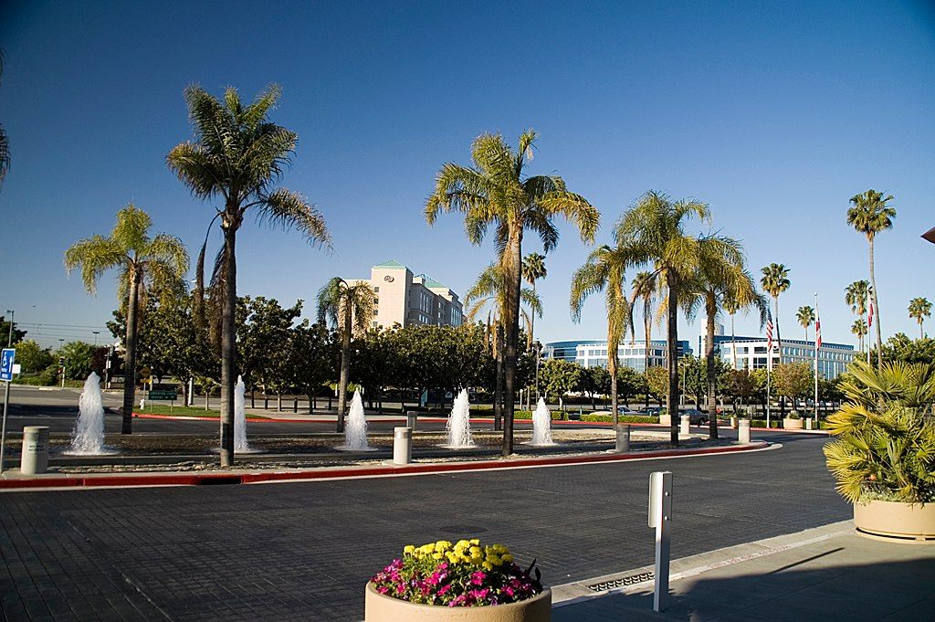 Fountains and palm trees along the entrance drive outside the Santa Clara Convention Center, with low office buildings beyond