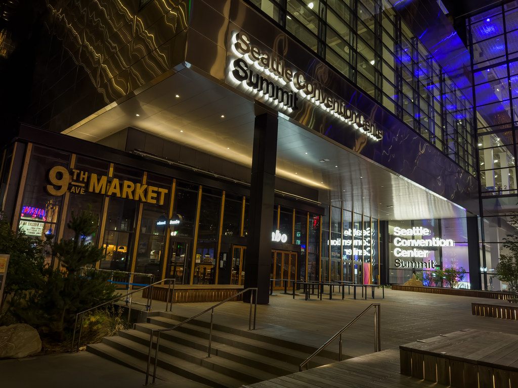 The lit entrance of the Seattle Convention Center Summit building at night, with its illuminated sign over the plaza steps
