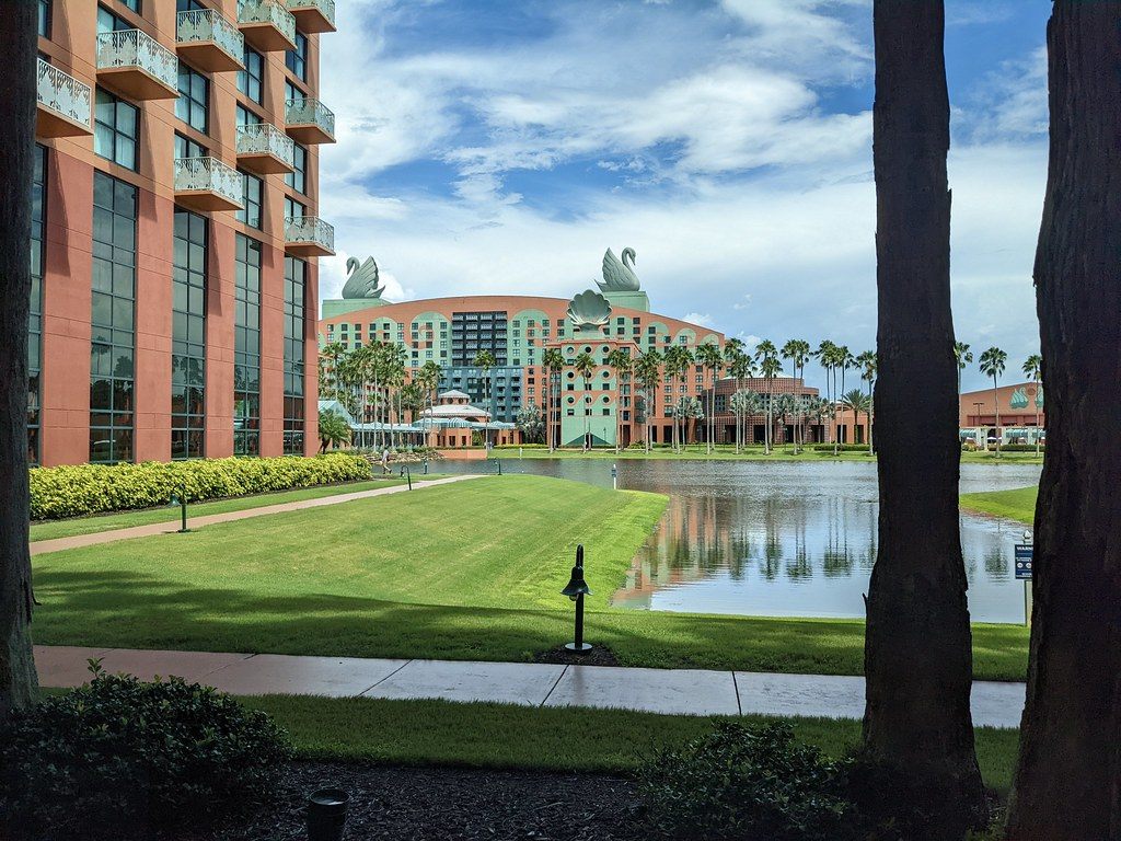 The coral and turquoise Swan hotel, crowned by two giant swan statues, seen across a lawn and a lagoon from the Dolphin, with a Dolphin wing at left