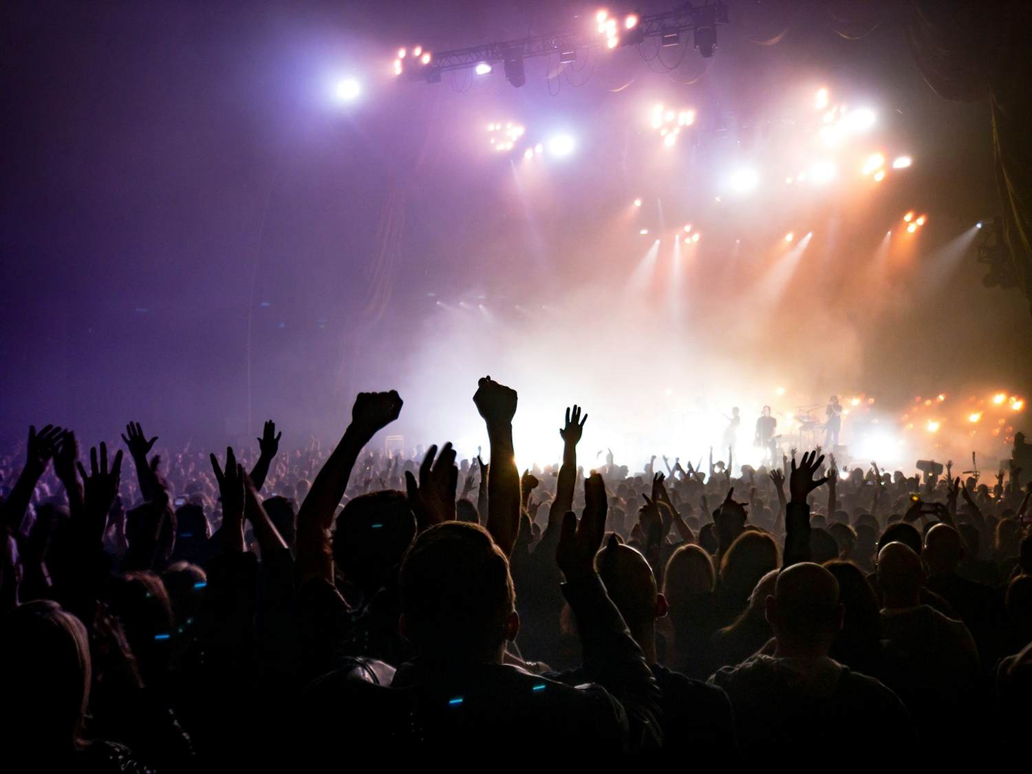 An arena crowd with hands raised under stage lights