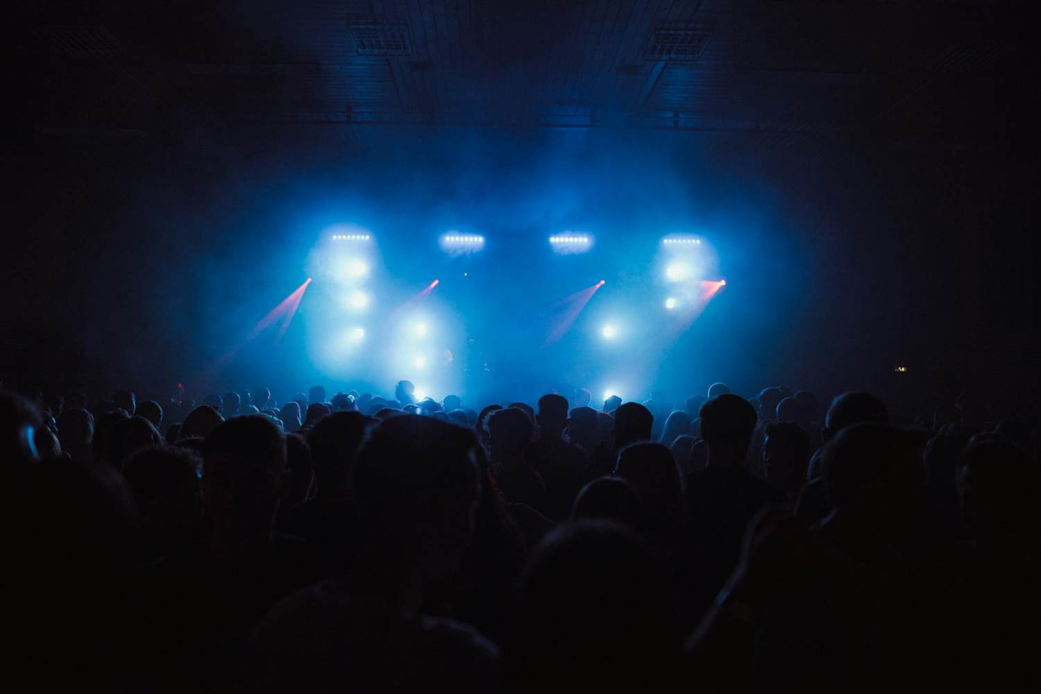 A crowd facing a stage lit in blue with beams of light
