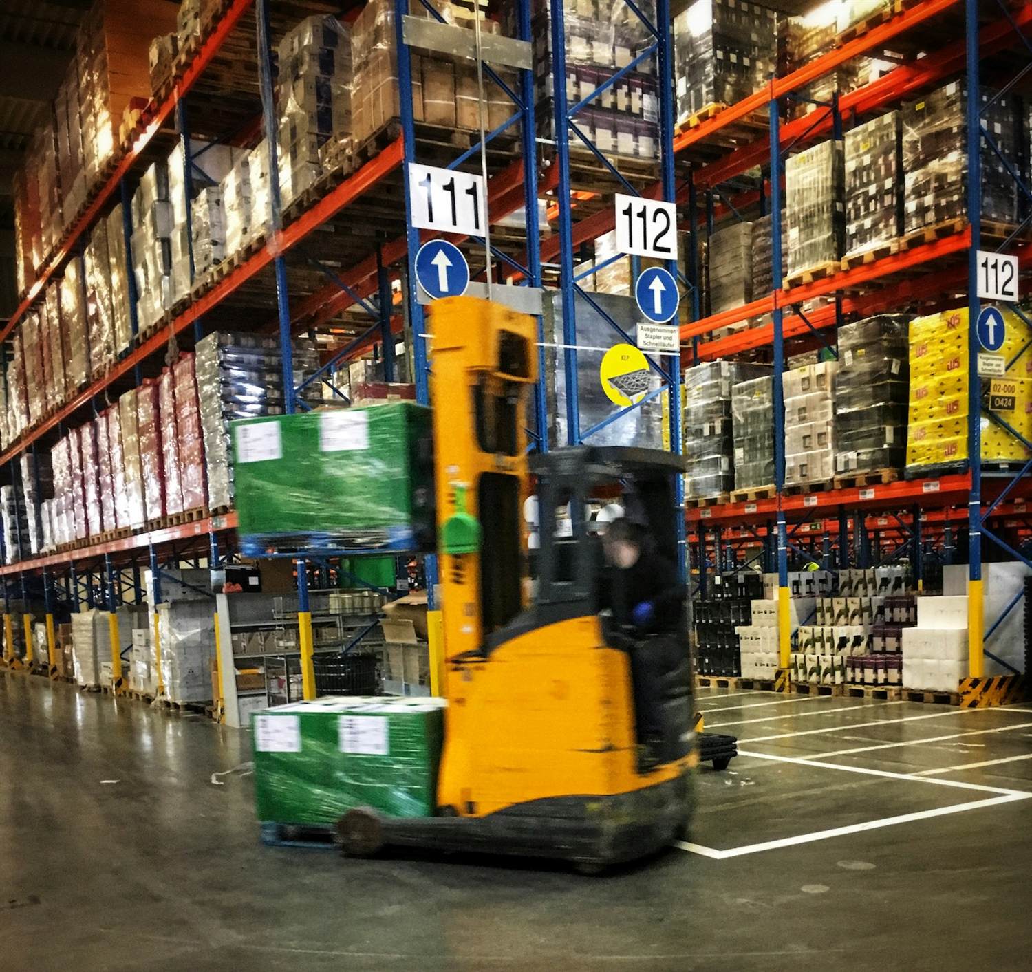 A forklift driving through a warehouse aisle stacked with pallets