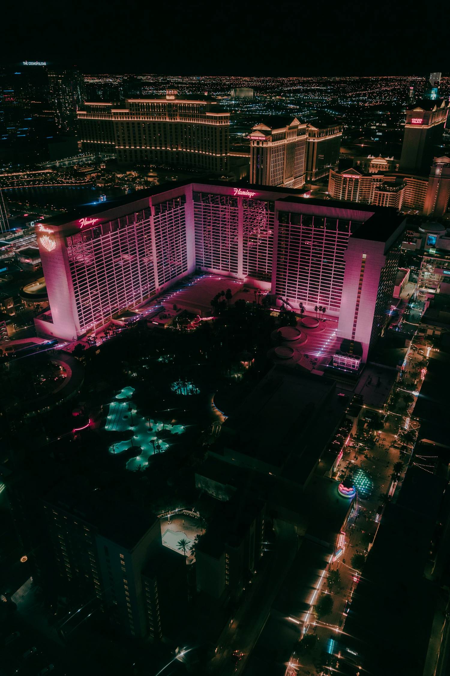 Aerial night view of the Flamingo hotel lit in pink with the Bellagio and Caesars Palace behind