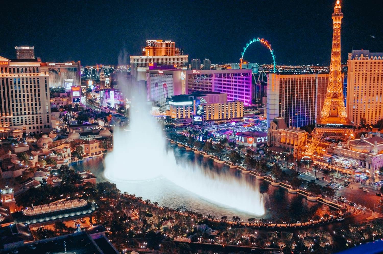 Aerial night view of the Bellagio fountains with the High Roller and Paris Eiffel Tower behind