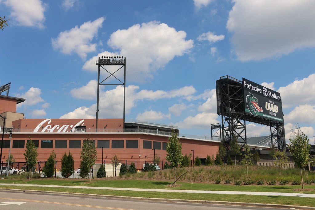 The brick wall and the Protective Stadium scoreboard tower on the BJCC campus, under a blue sky