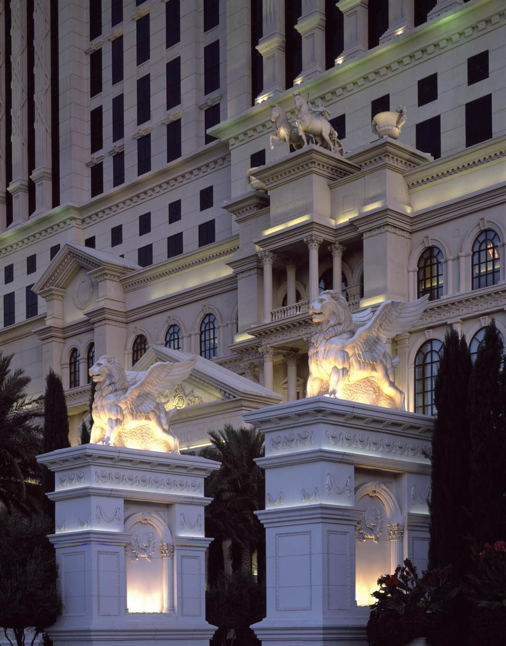 Winged lion statues lit at dusk in front of the Caesars Palace tower