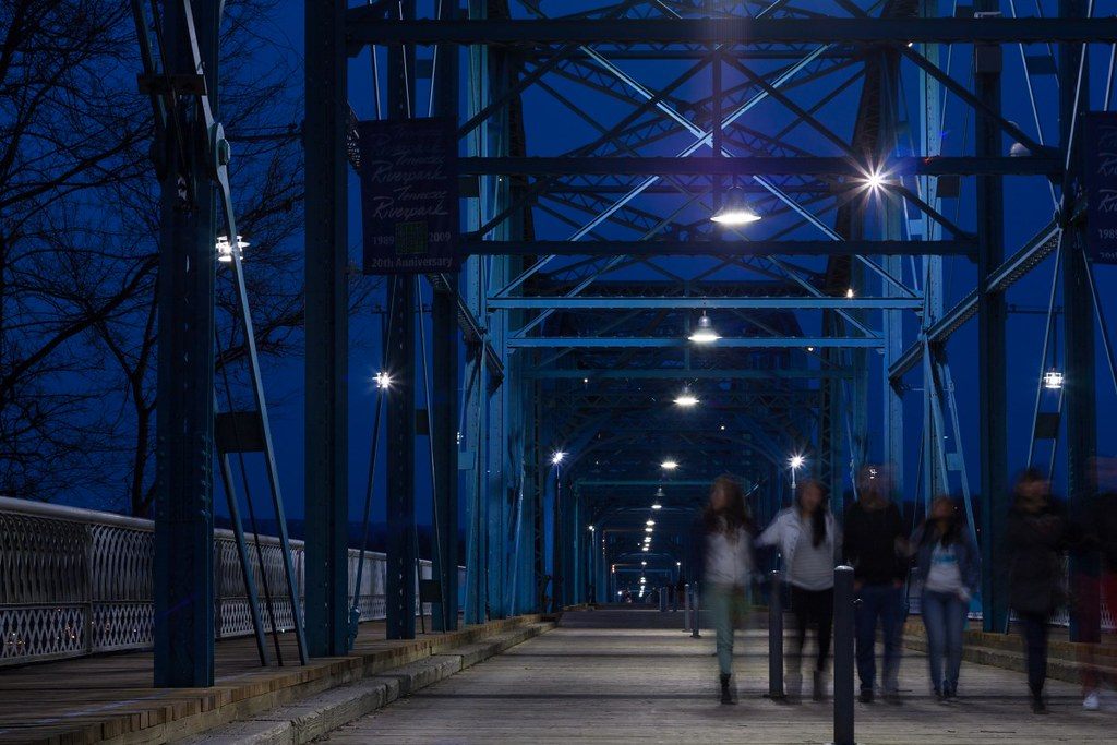 People walking across the blue steel trusses of the Walnut Street pedestrian bridge in Chattanooga at dusk