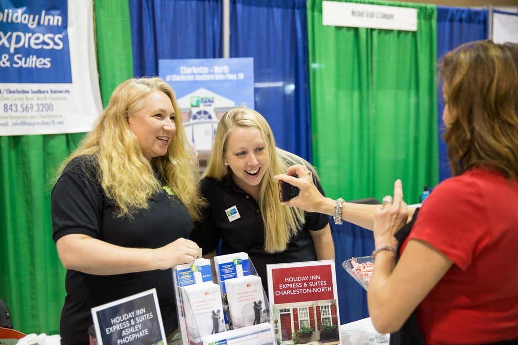 Exhibitors laughing with a visitor at a hotel booth with brochures on the table, North Charleston Business Expo