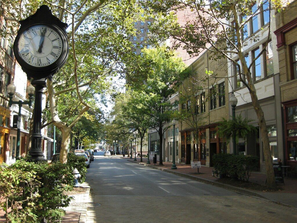 Tree-lined Capitol Street in downtown Charleston, with a black post clock, brick sidewalks and storefronts in older brick buildings