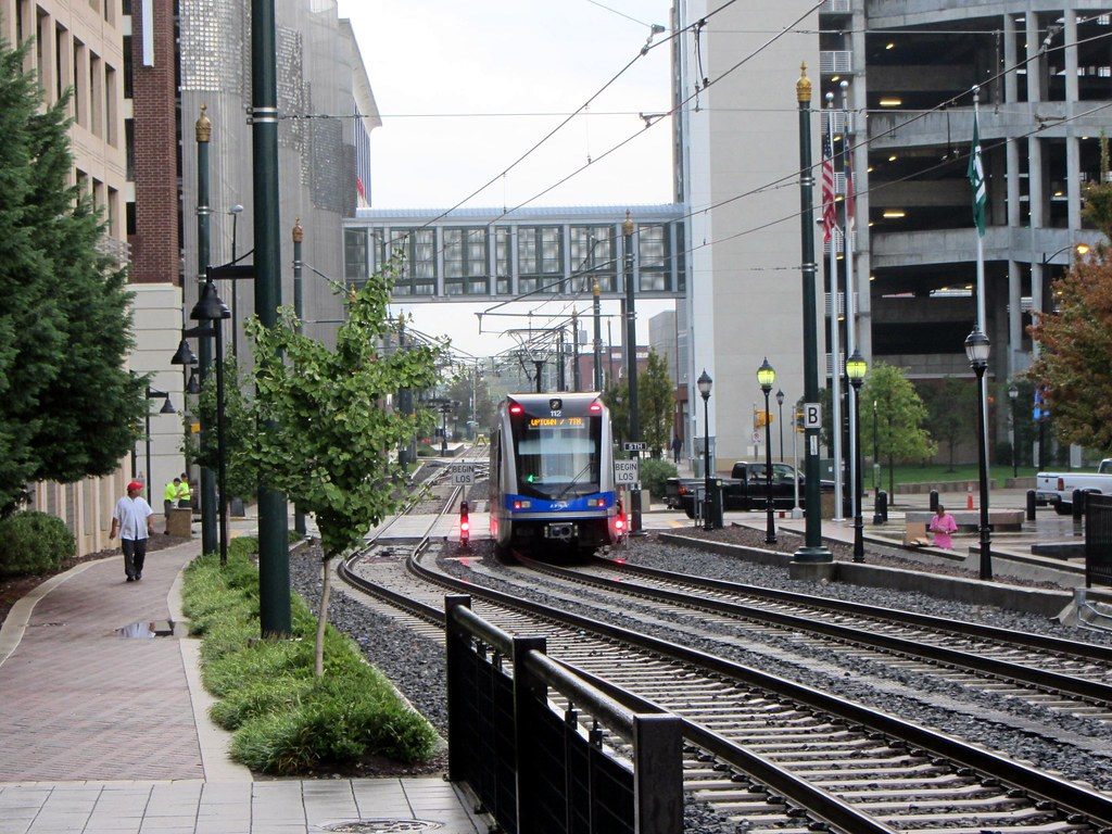A LYNX light rail train running between landscaped tracks under a glass skybridge in Uptown Charlotte