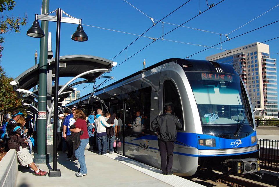 A silver and blue LYNX Blue Line train boarding passengers at an elevated station platform in Uptown Charlotte