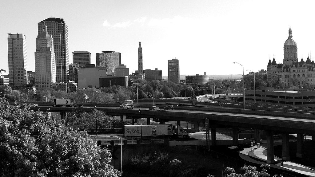 Black-and-white view of trucks on elevated highway ramps in front of the downtown Hartford skyline and the State Capitol dome