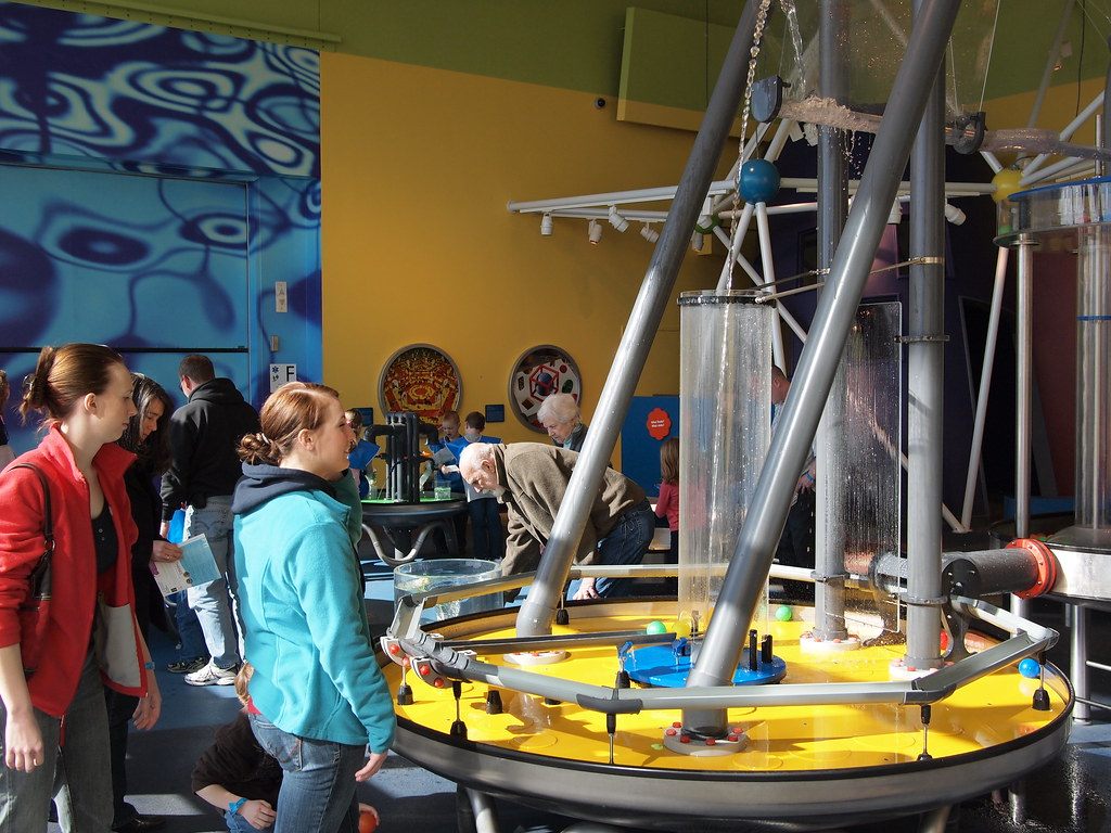 Visitors around a yellow water-table exhibit with steel poles inside the Connecticut Science Center