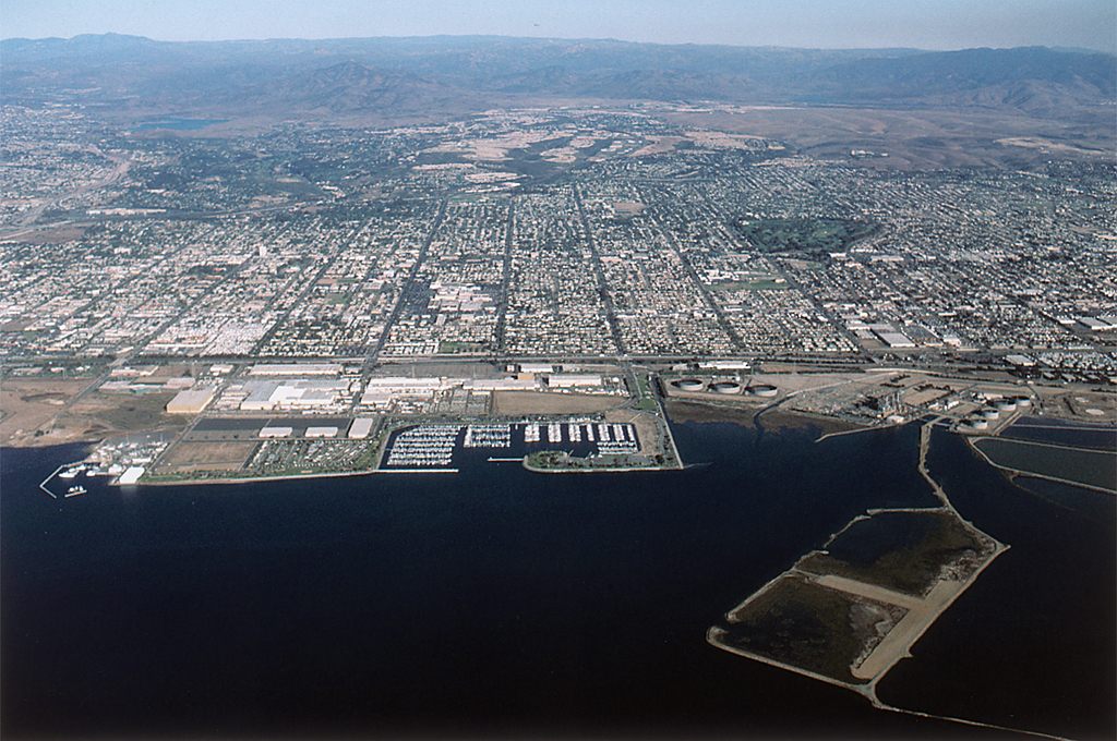 Older aerial photo of the Chula Vista waterfront on south San Diego Bay: a small marina, industrial land and open bayfront parcels, with the city spreading inland to the hills