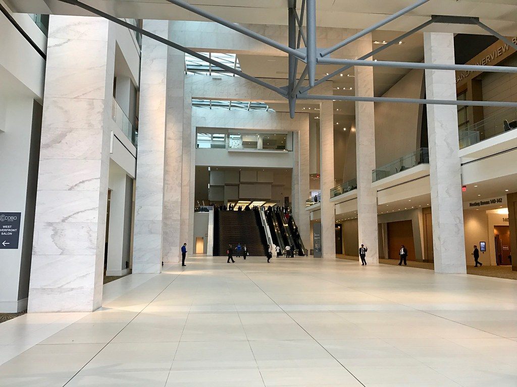 A tall white marble atrium with escalators at the far end and meeting room signs along an upper balcony
