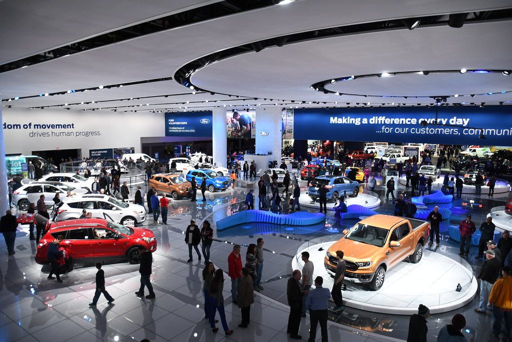 The Ford exhibit at the 2018 Detroit auto show seen from above, with vehicles on round turntables under large suspended ceiling rings and banner screens
