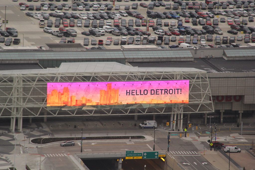Cars parked on the convention center's roof deck above an LED screen reading Hello Detroit on the bridge over Jefferson Avenue