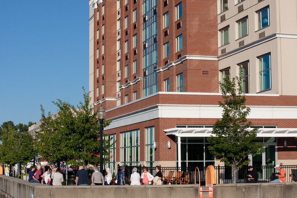 Visitors gathered along the pier promenade below the brick base and glass stair tower of the Bayfront Landing hotel and convention center