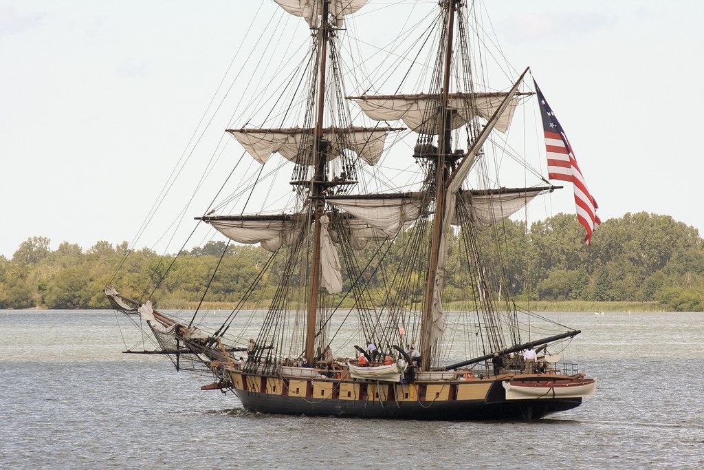 The square-rigged U.S. Brig Niagara under sail on Presque Isle Bay, flying a large American flag, during the tall ships welcome parade