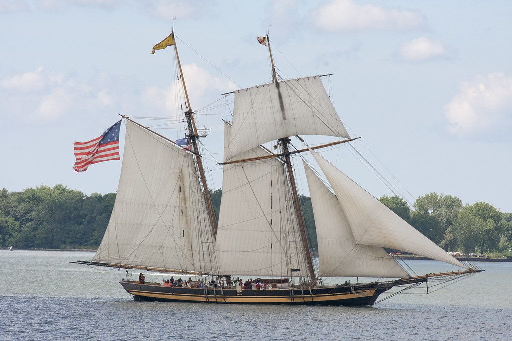 A two-masted topsail schooner with passengers on deck sailing across Presque Isle Bay in the tall ships parade