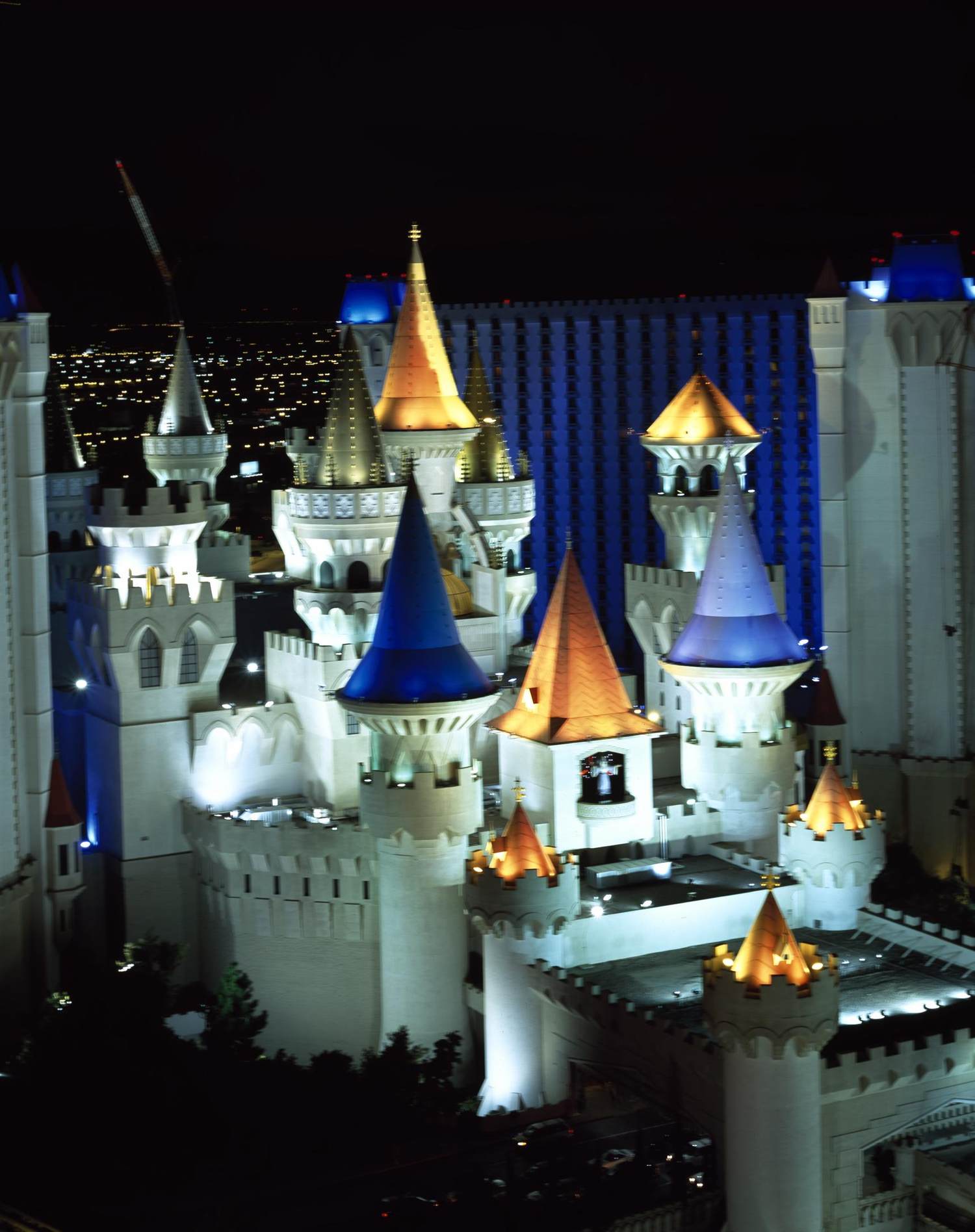 The lit turrets of the Excalibur castle at night with the Luxor tower behind