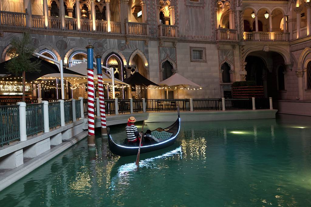 A gondolier in a striped shirt rows a gondola on the Venetian canal at night