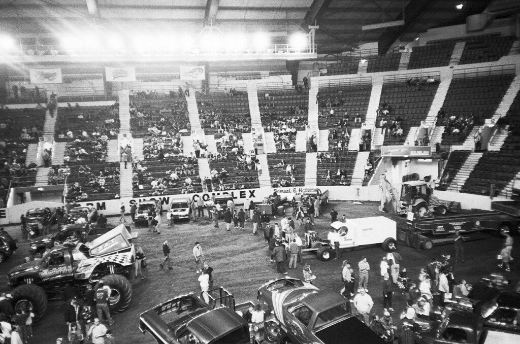Pickup and monster trucks on the floor of the Farm Show arena with spectators in the stands