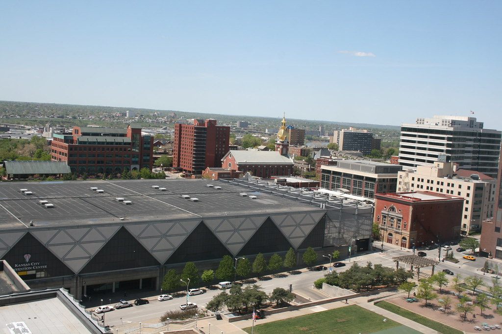 The long dark roof of the Kansas City Convention Center seen from a tall building, with its triangle-patterned facade above the street and downtown brick buildings beyond